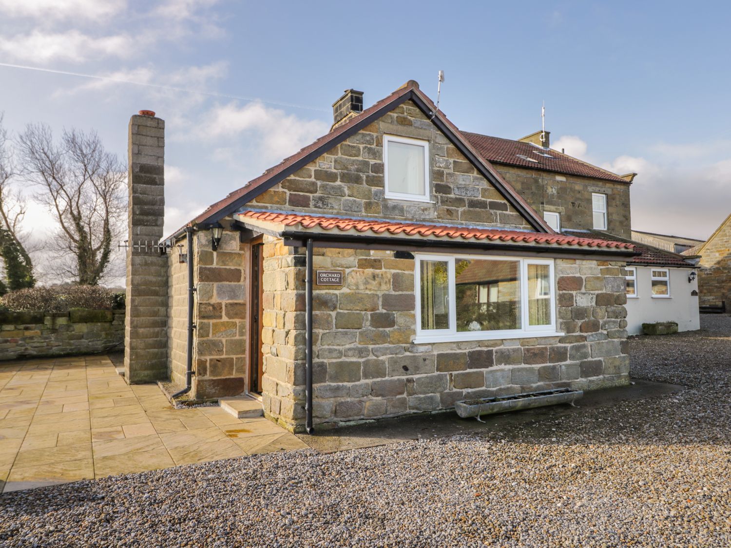 A stone cottage with a tiled roof and chimney surrounded by gravel and paved paths at Orchard Cottage in Robin Hoods Bay