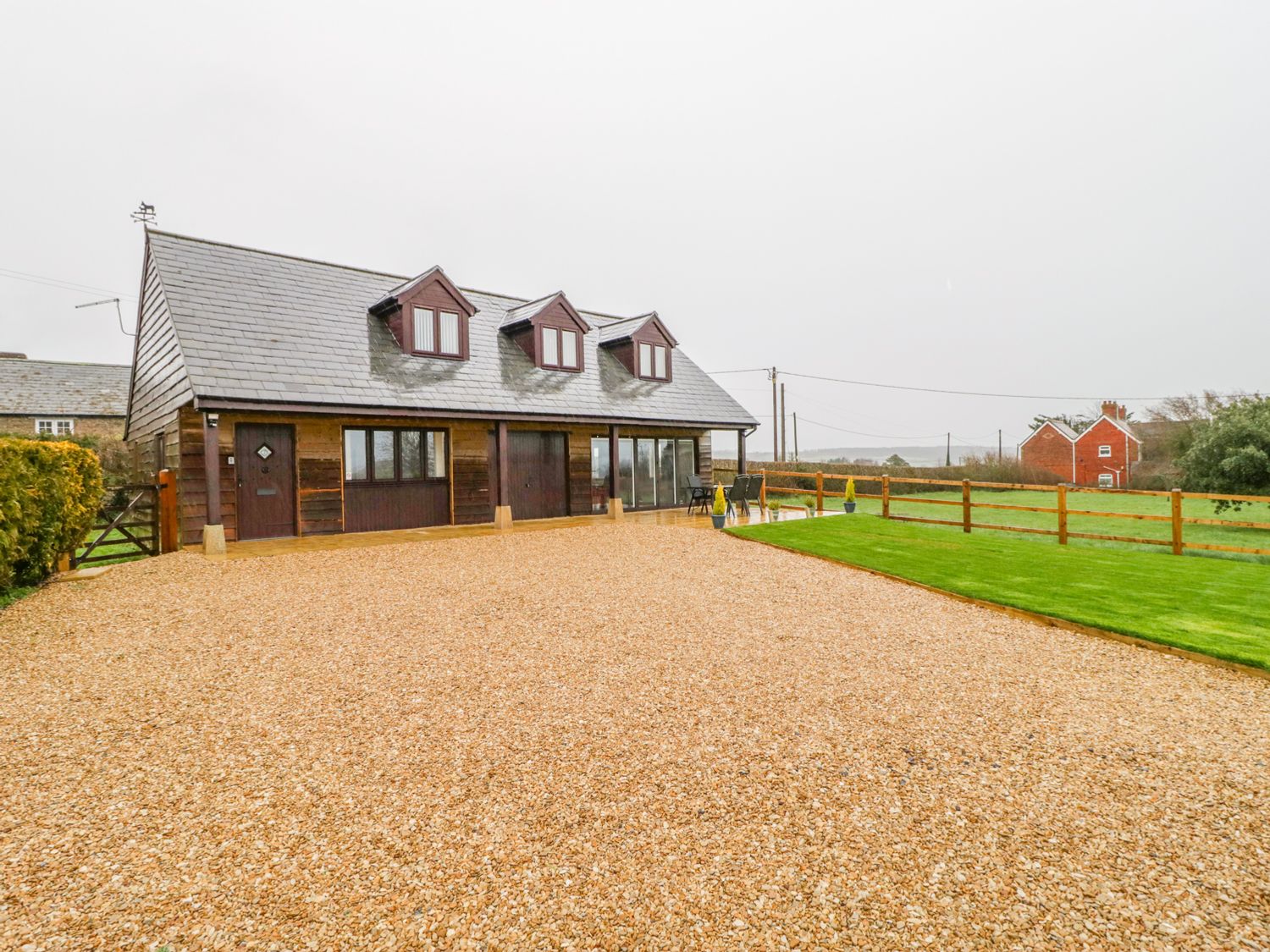 A wooden house with three dormer windows a gravel driveway and a fenced grassy area at The Donkey Shed in Sherborne
