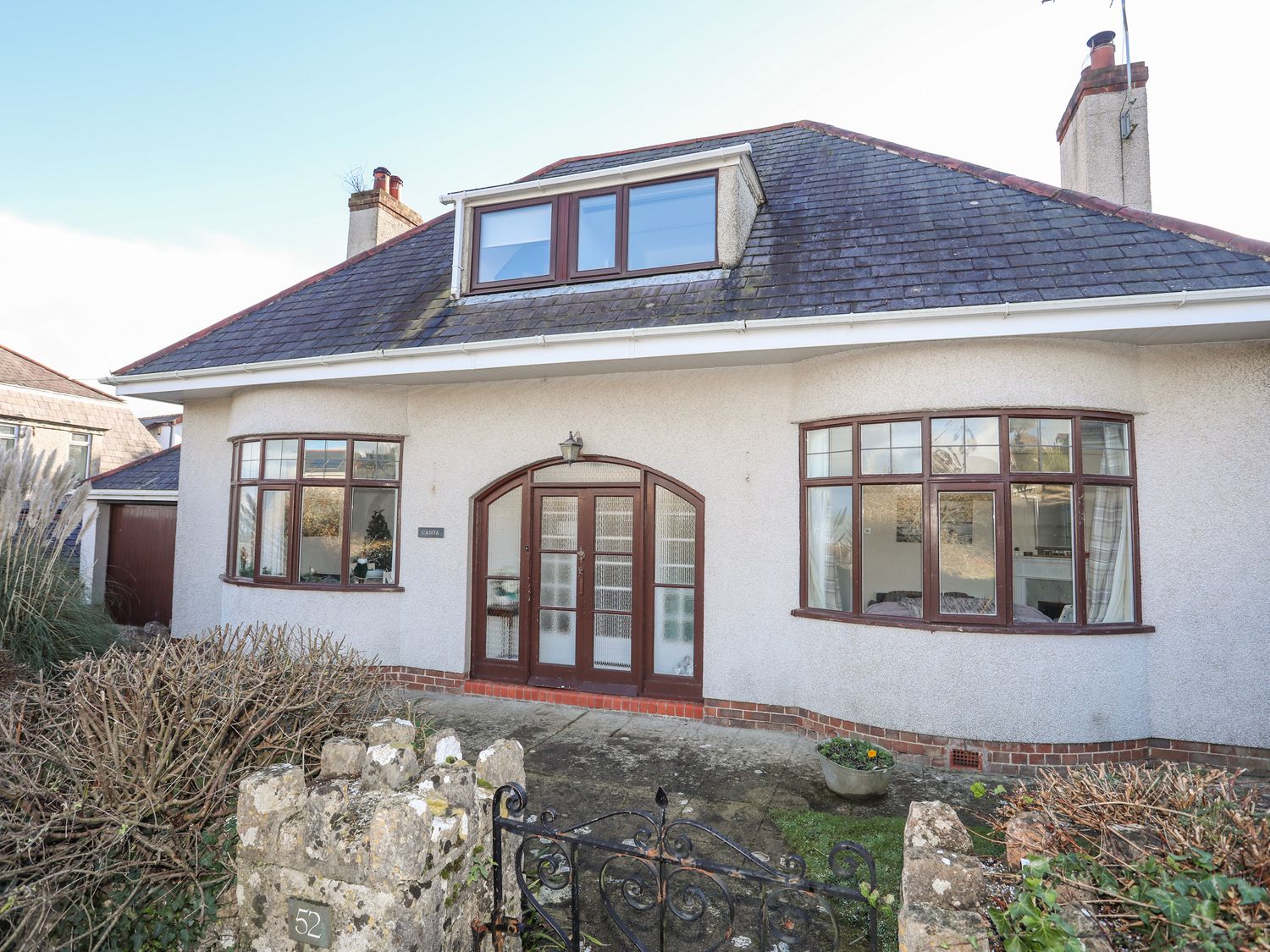 The front exterior of a two-story house with arched double doors and bay windows at Casita in Benllech