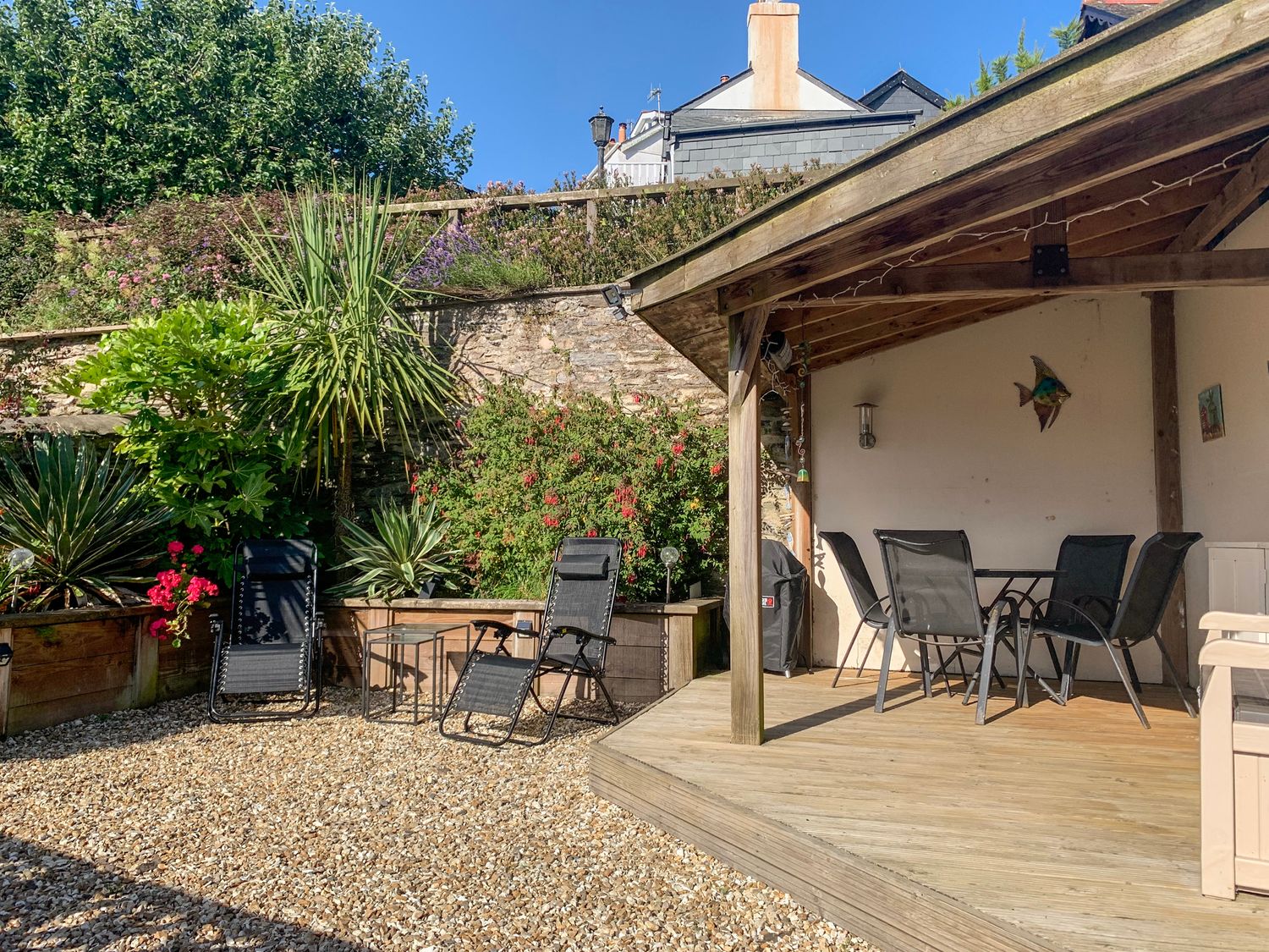 An outdoor seating area with black chairs under a wooden pergola and additional black chairs with a small table on a gravel surface at Simples in Dartmouth