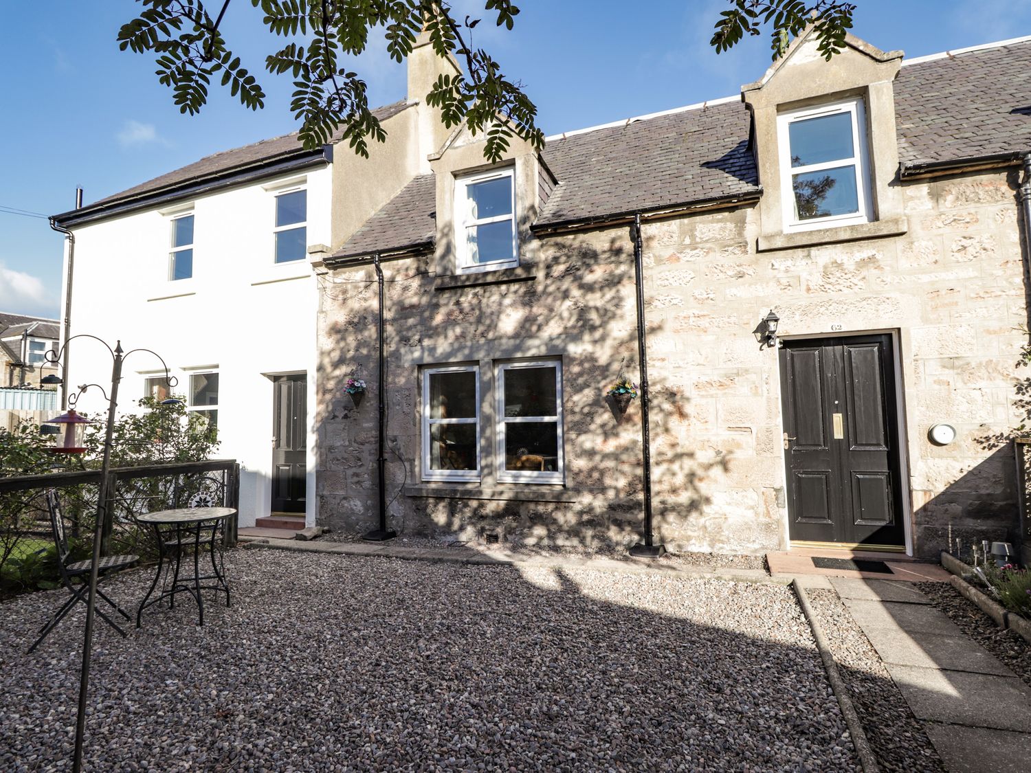 A stone and white house exterior with black doors and windows and a gravel yard with a small metal table and chairs at 62 Society Street in Nairn