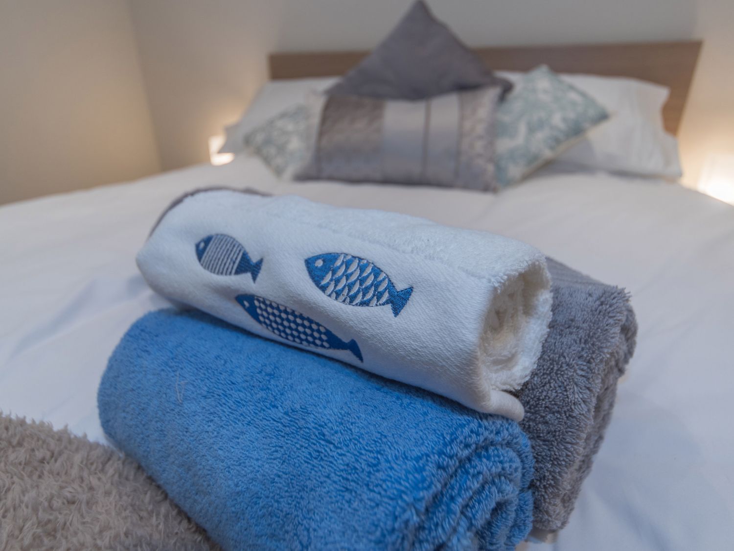 A bed with folded towels on it and decorative pillows in the background at Seashells Cottage in Lytham St Annes