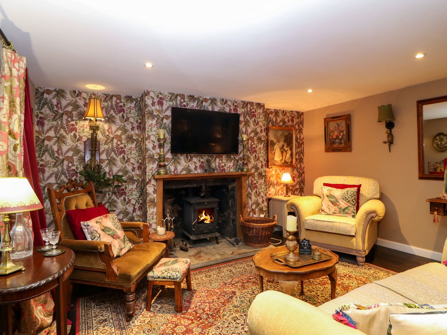 A living room with floral wallpaper a fireplace a TV armchairs and a coffee table at Wonderland Cottage in Newburgh Fife