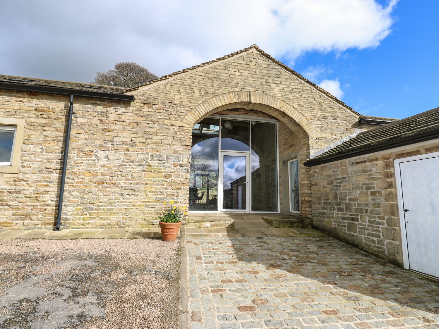 Stone exterior wall of a building with an arched glass door and cobblestone driveway at 2 Barn Cottages in Norwood Green