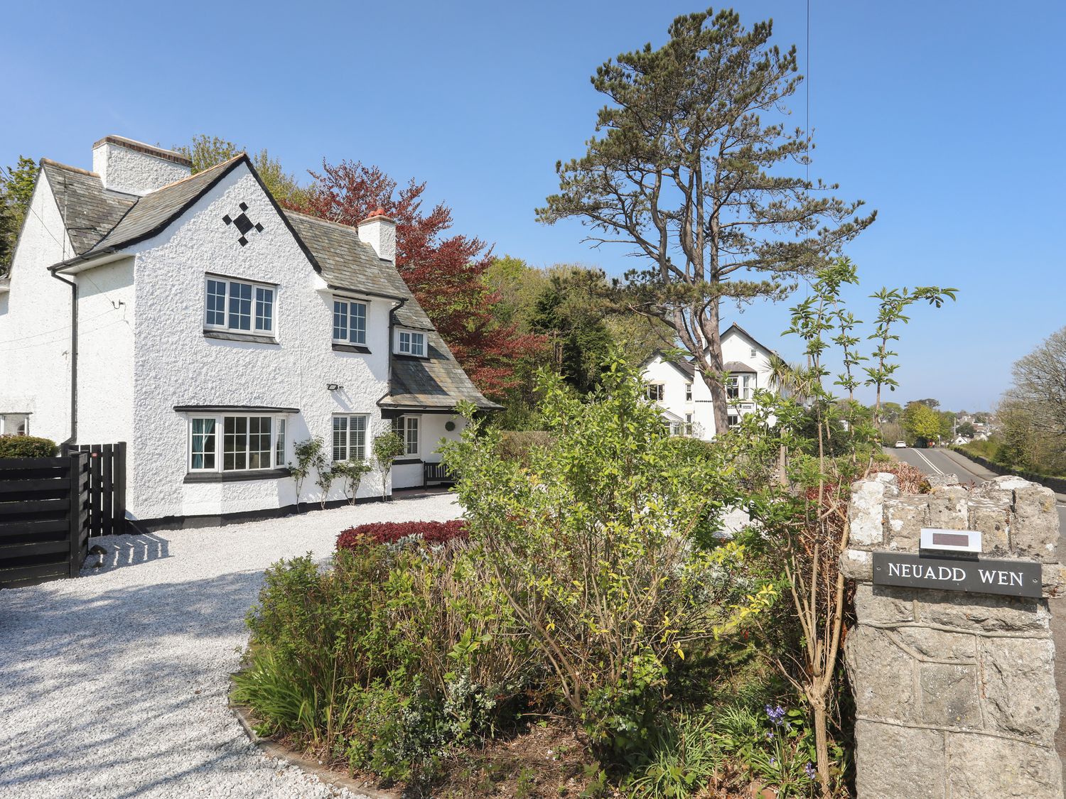 A white house with a gravel driveway surrounded by trees and bushes at Neuadd Wen in Benllech