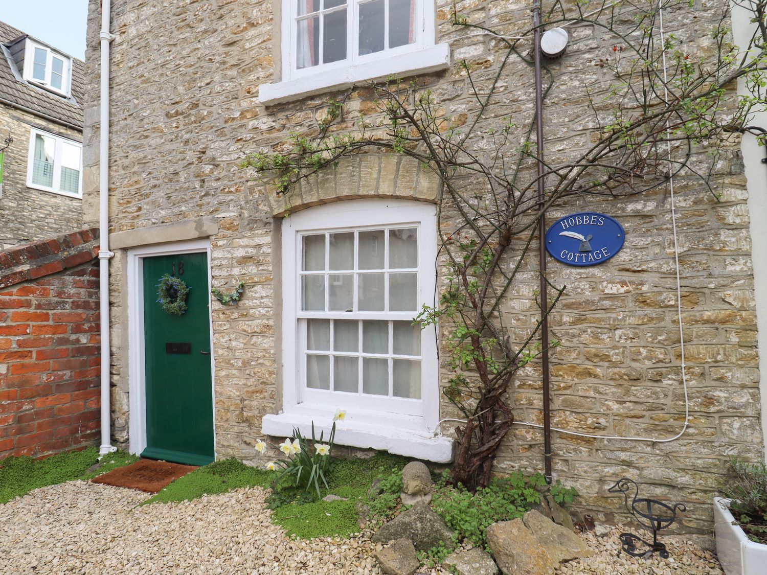 Stone cottage exterior with green door wreath window and climbing plant at Hobbes Cottage in Malmesbury