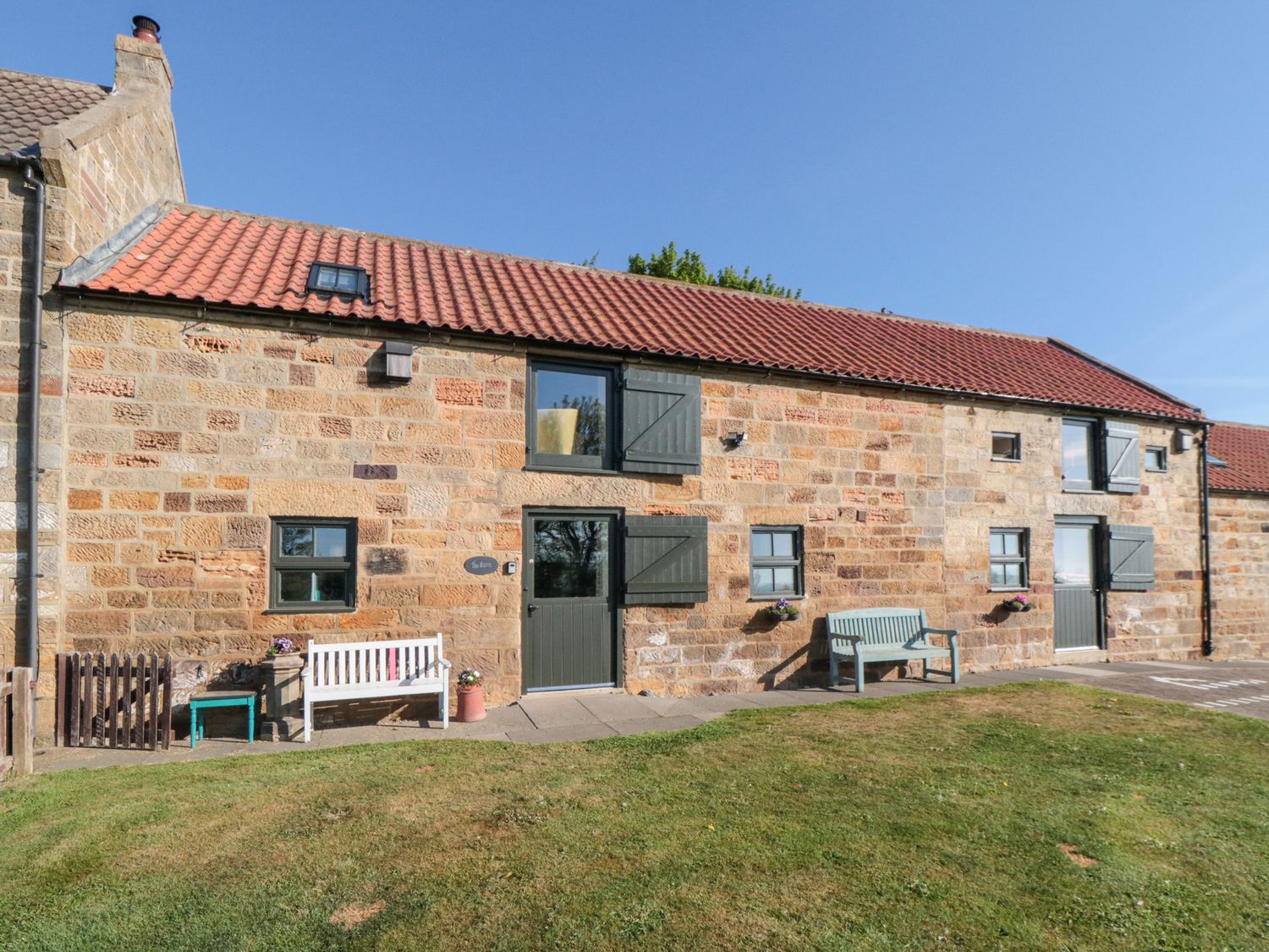 A stone exterior of a house with green doors and windows with benches on a lawn at The Barn in Staithes