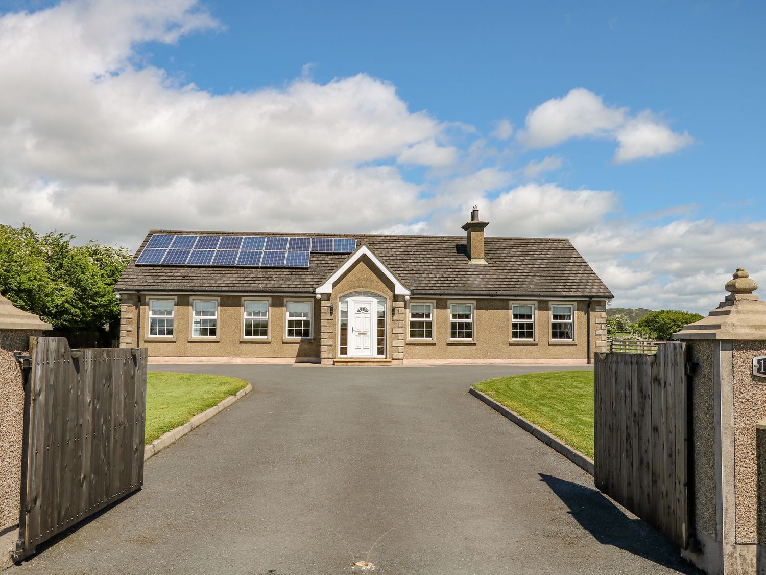 A single story house with solar panels on the roof a paved driveway and wooden gates at Willow Tree Farm House in Newry near Jonesborough