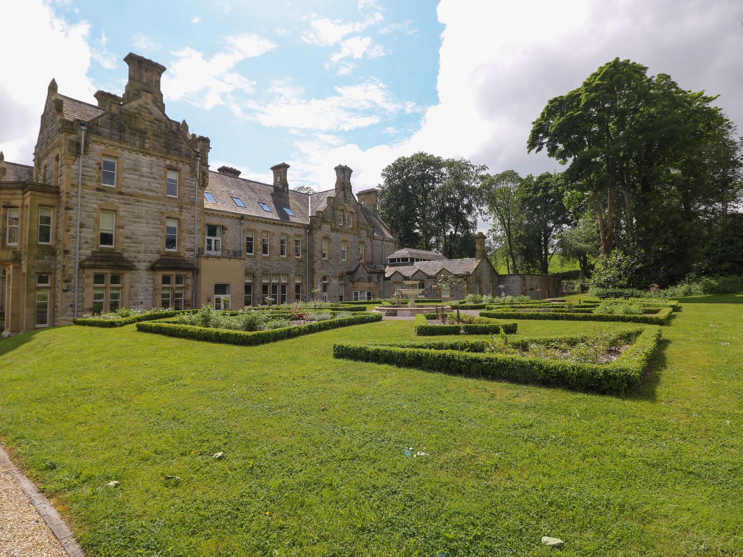 A large stone mansion with a manicured garden and hedges in front at The Violet Suite Stone Cross Mansion in Ulverston
