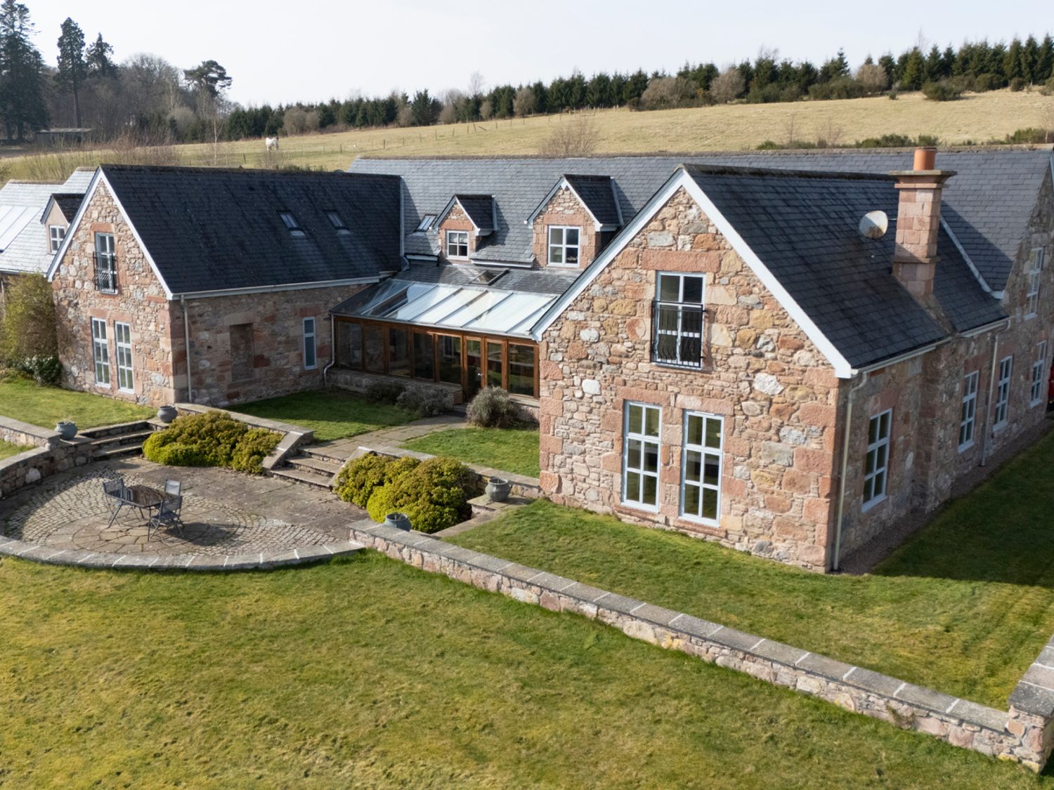 A stone house with multiple windows and a patio with outdoor furniture surrounded by a grassy lawn at Quarryfield in Munlochy