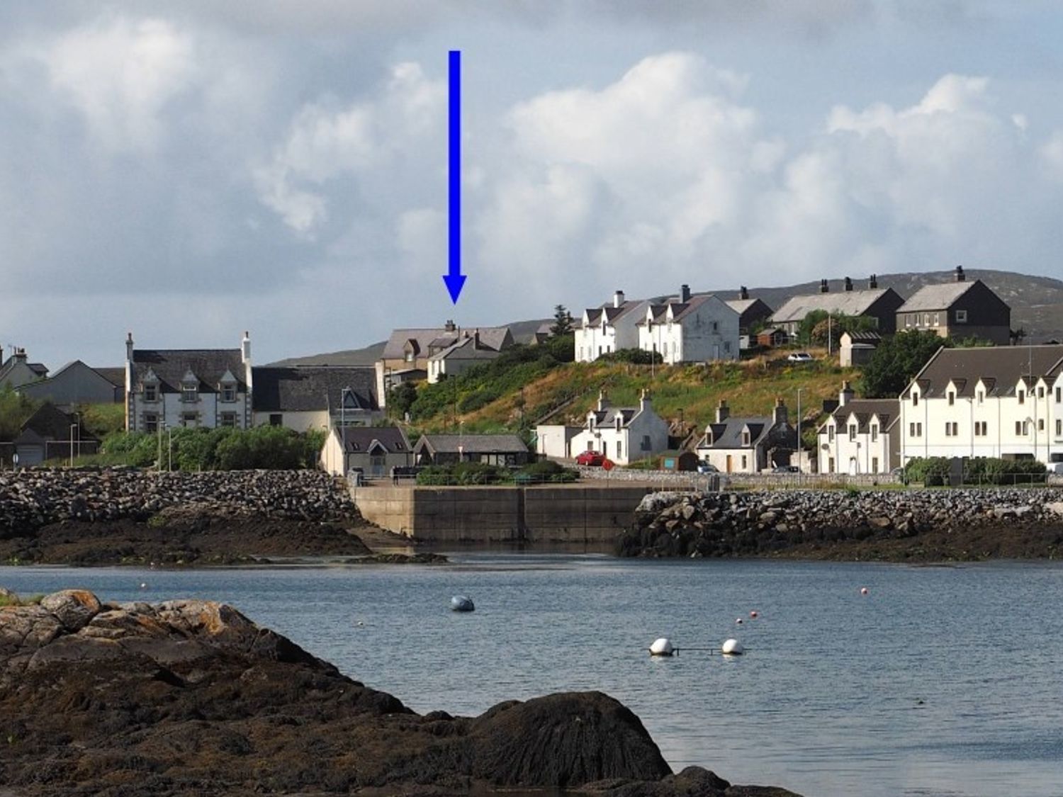 A coastal village with houses on a hillside and a stone pier in the water at Tulloch House in Lochboisdale