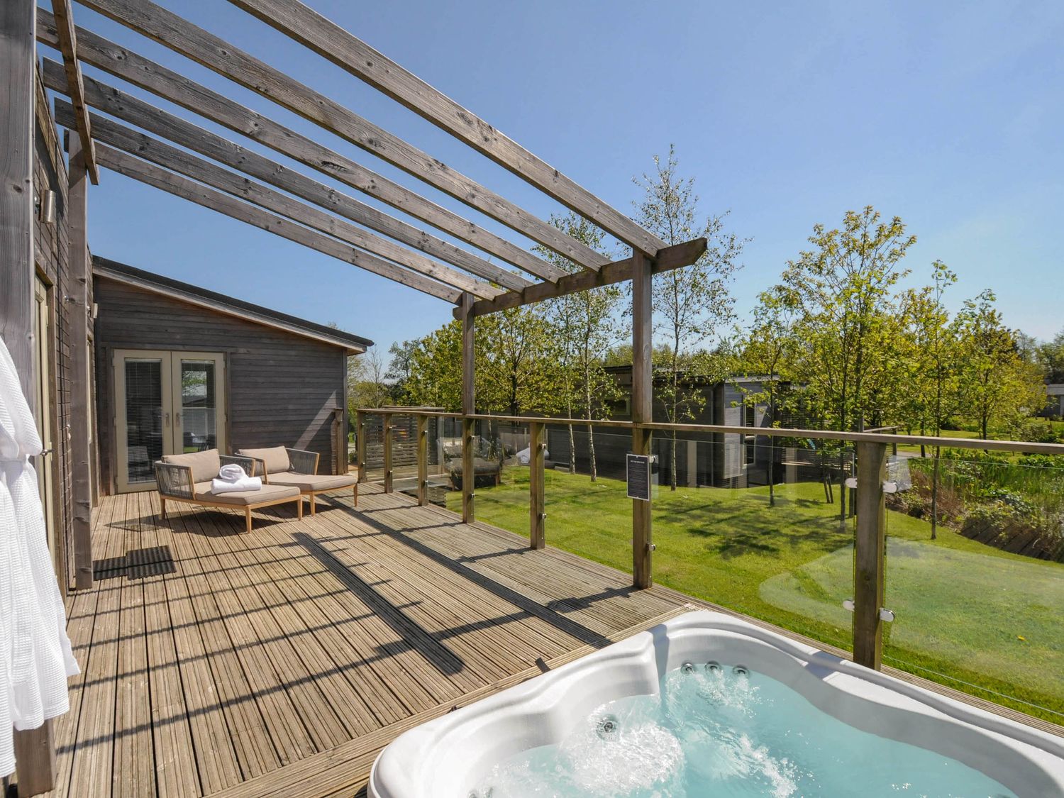 A wooden deck with a hot tub a lounge chair and a wooden pergola overlooking a garden at 11 Meadow Retreat in Dobwalls