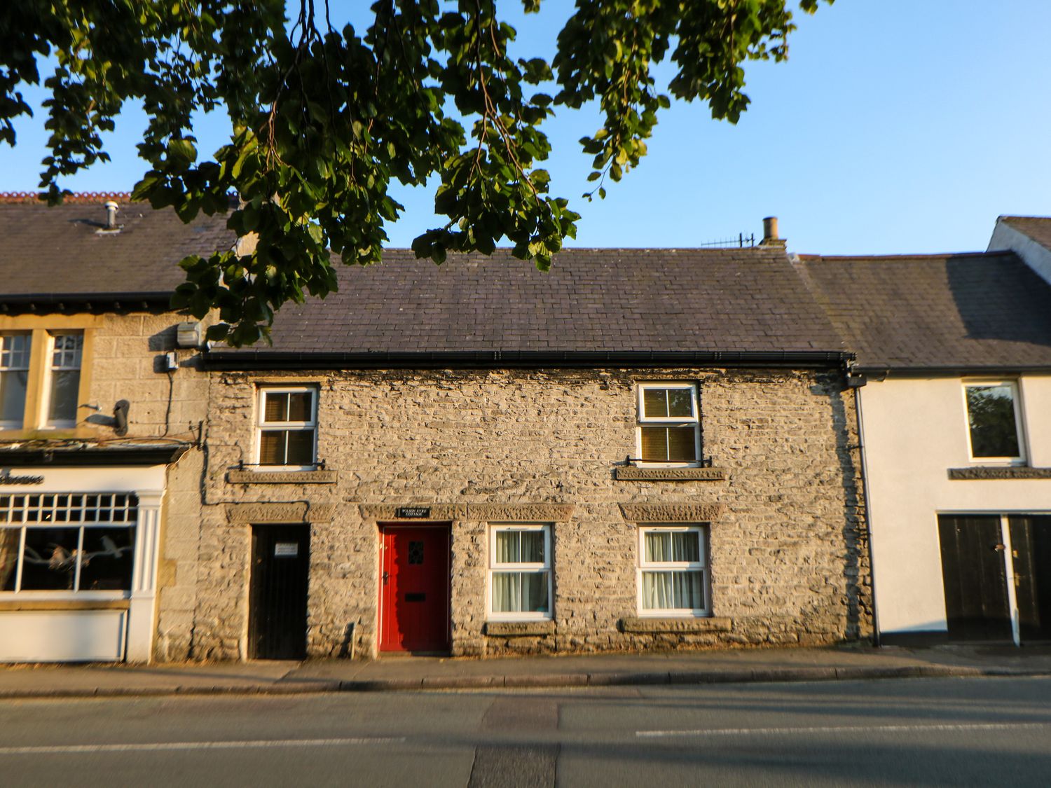 A stone facade house with a red door and four windows along a street at Wilson Eyre Cottage in Castleton Peak District