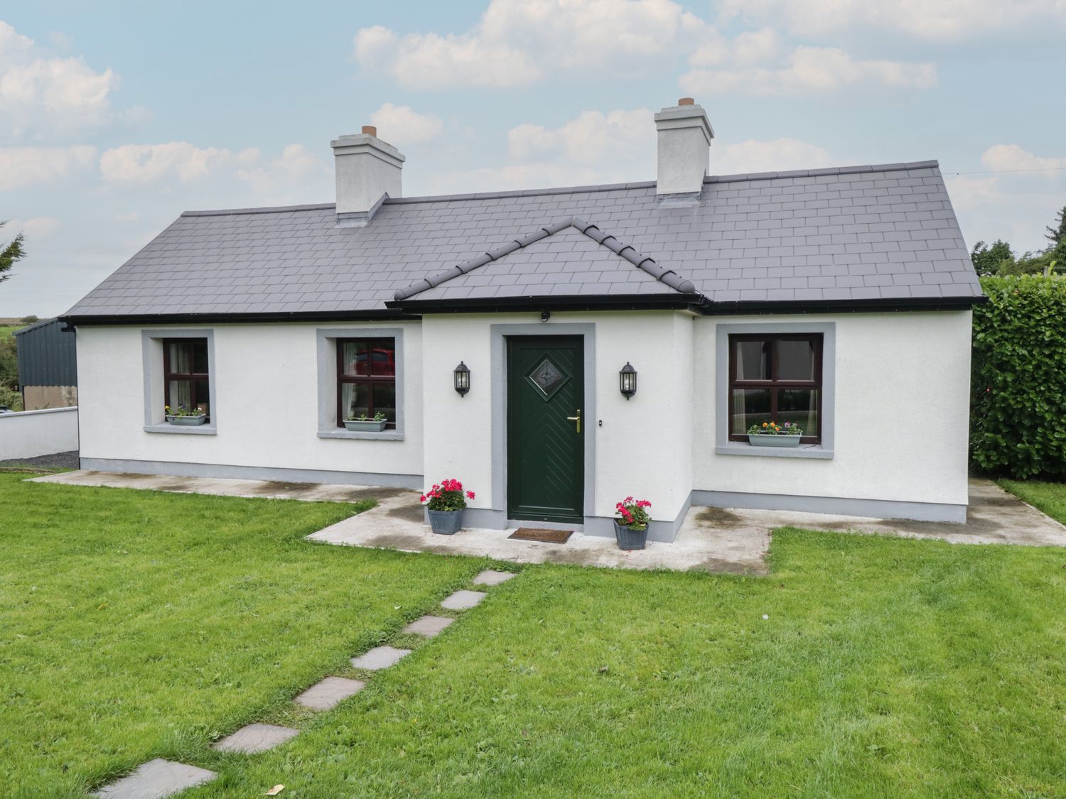 A single story house with a dark green front door two chimneys and a lawn with stepping stones at Kates Cottage Killawullaun near Ballintubber County Mayo