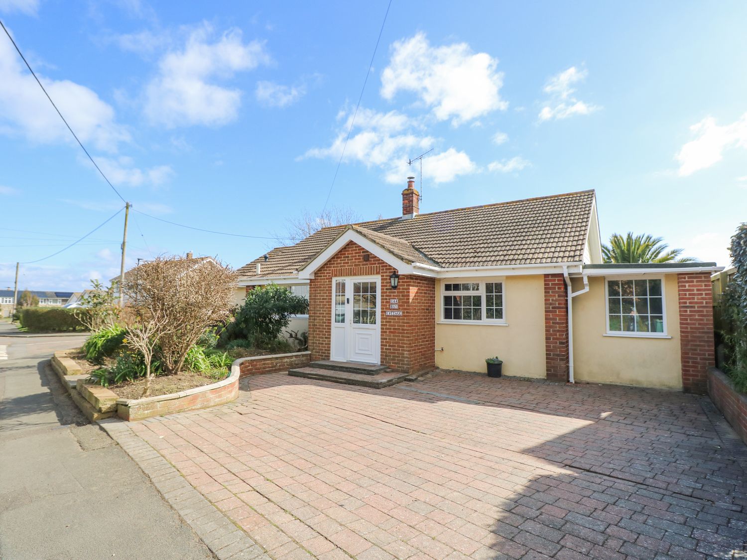 A single story house with a brick and beige exterior and a tiled roof with a paved driveway and a small garden bed at Bay Cottage in Bembridge