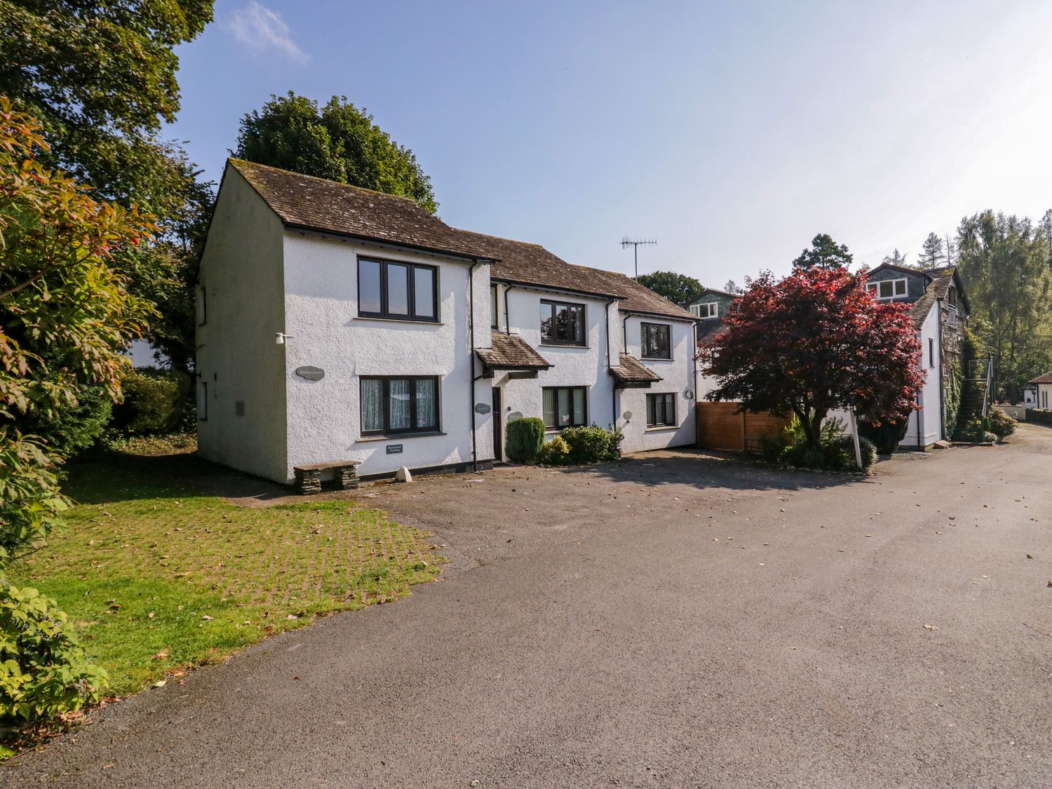 A white two story house with multiple windows and a red tree in front with a driveway at Buttermere in Ambleside