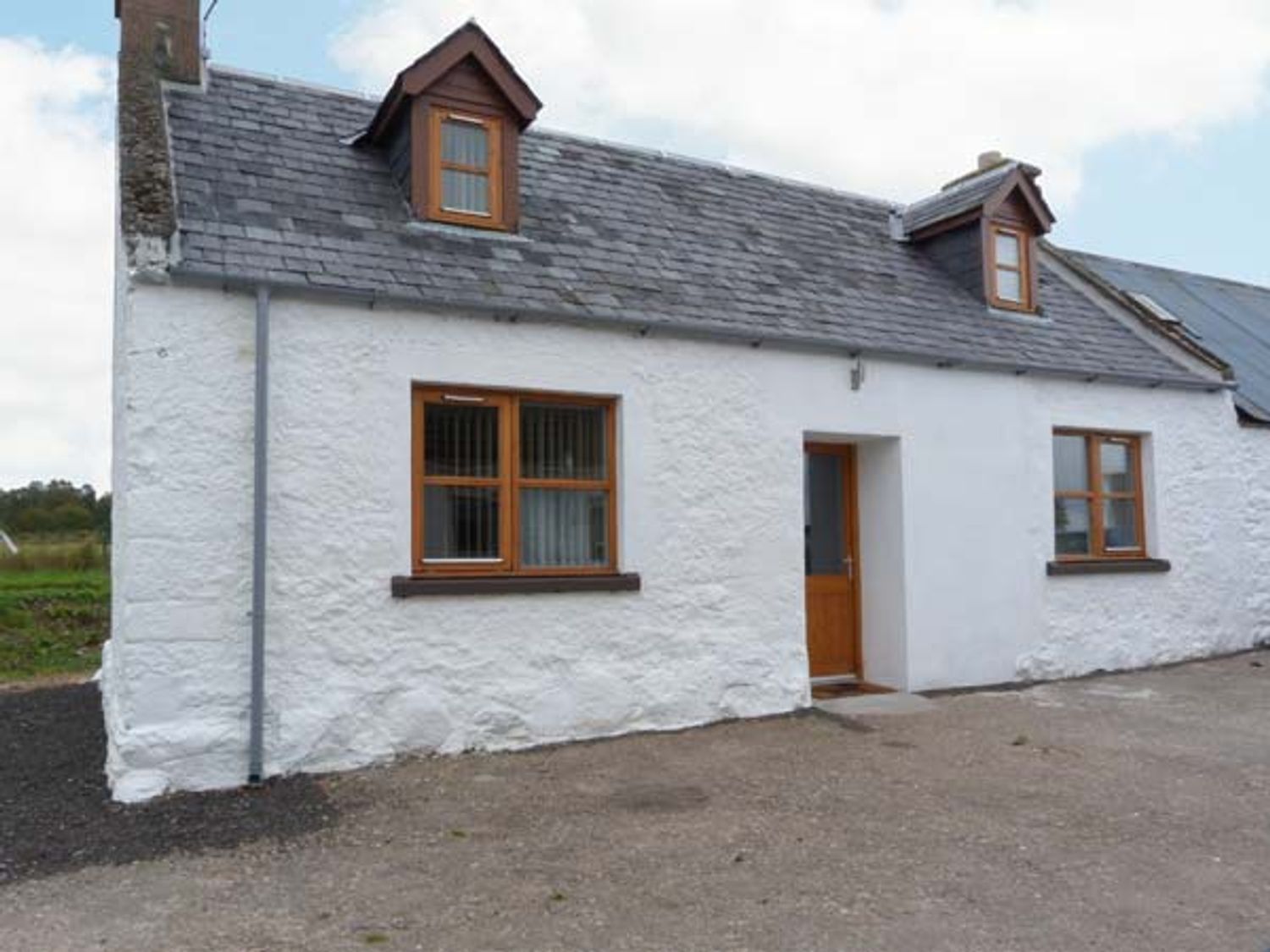 An exterior view of a white stone house with wooden framed windows and a door at The Croft House in Muir of Ord near Beauly