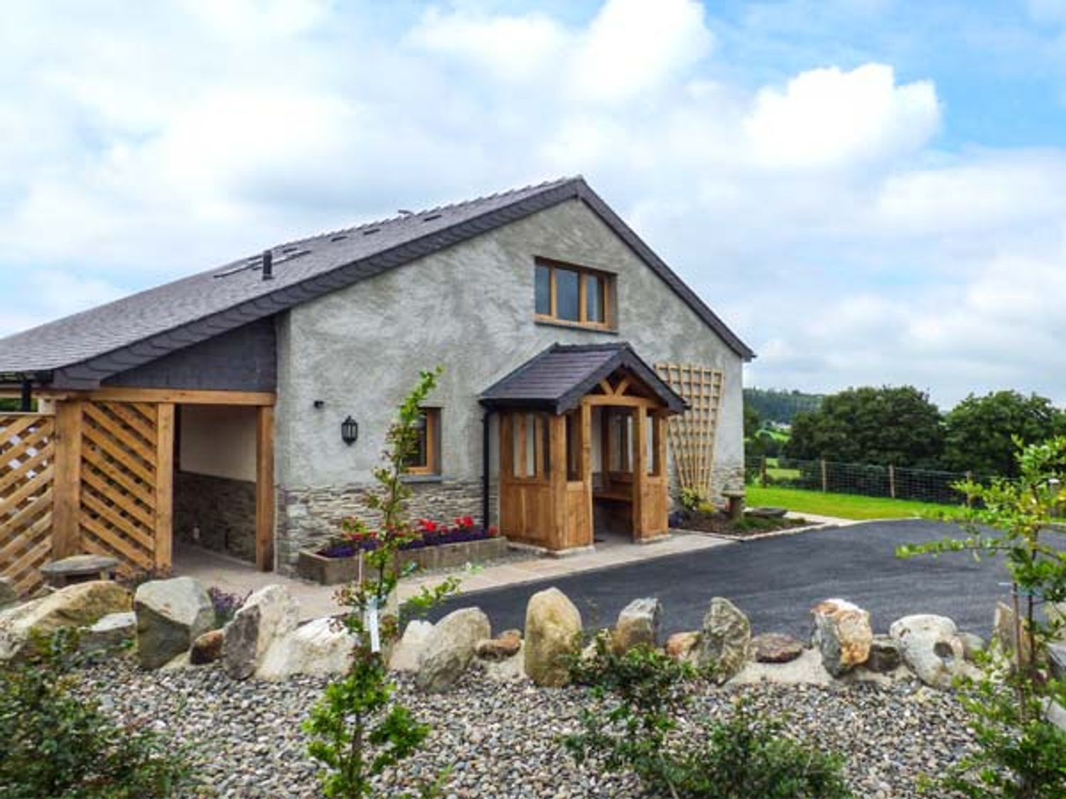 An exterior view of a house with a stone and wood entrance and a garden with rocks and plants at Tyn Y Celyn Uchaf in Clocaenog near Ruthin
