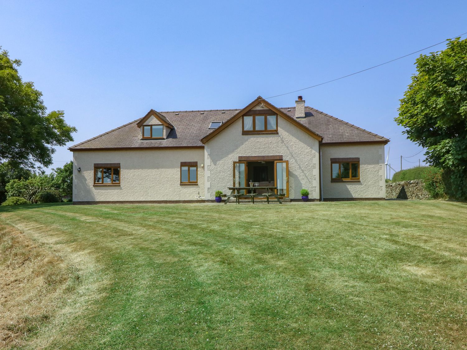 A white house with brown window frames and a garden with a picnic table at Fferam Y Llyn in Rhosgoch near Cemaes Bay