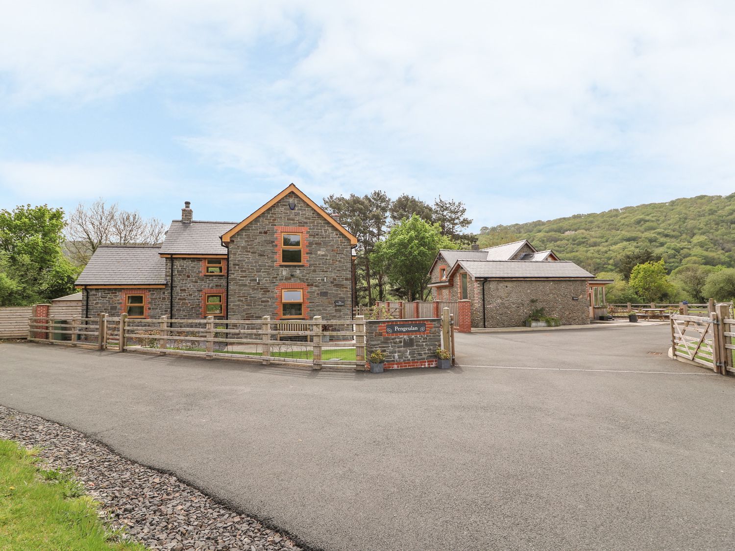 Two stone houses with slate roofs and fenced yards on a paved driveway with hills in the background at The Farmhouse in Capel Bangor near Aberystwyth