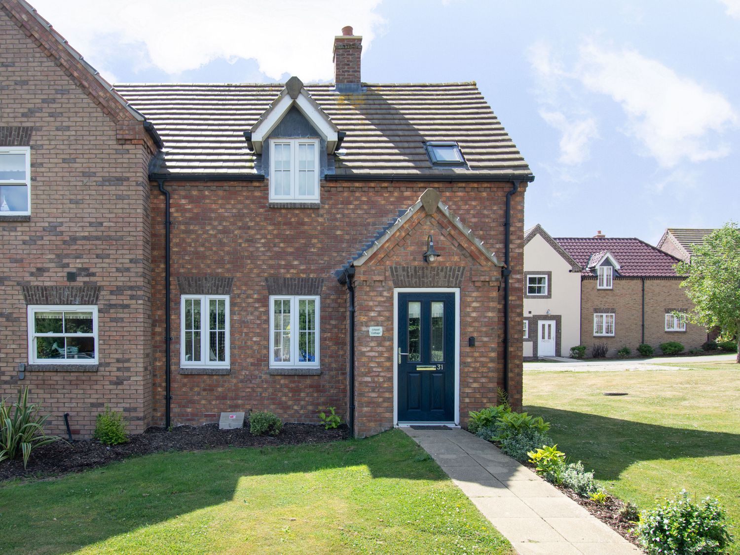 A brick house with a blue front door and white windows with a garden and pathway in front at Lilipad Cottage The Bay near Filey