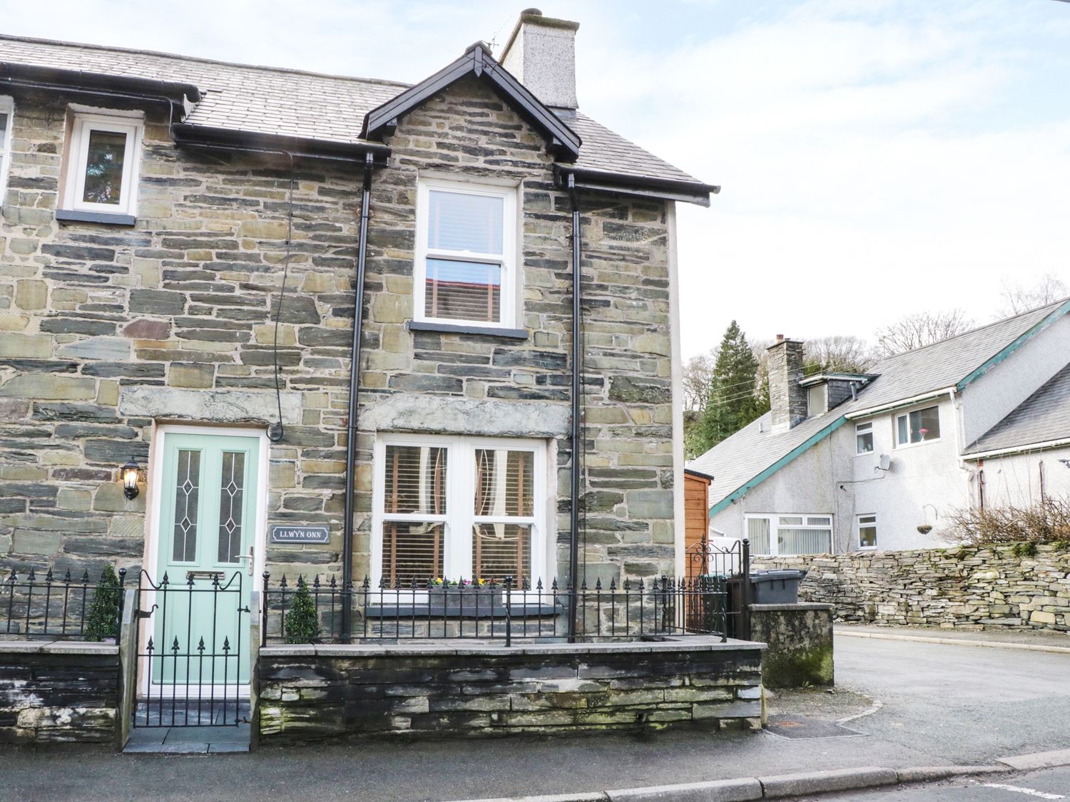 Stone house with a light green door and small front garden with iron fence at Llwyn Onn in Dolwyddelan