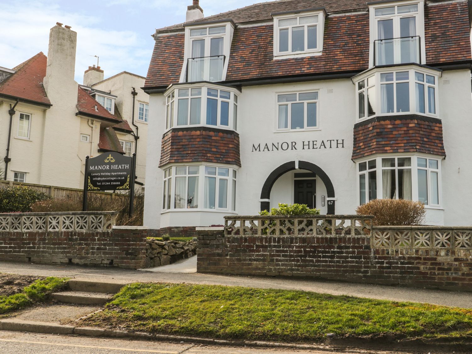 The exterior of a white building with brown tiled roof and bay windows with a sign for Manor Heath luxury holiday apartments in Scarborough