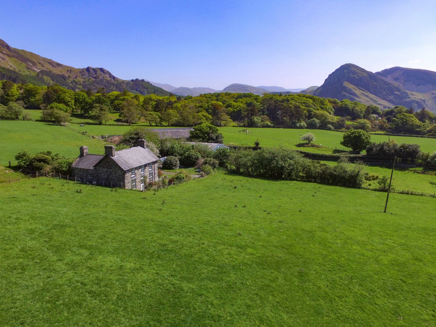 A stone house surrounded by green fields trees and mountains in the background at Peniarth Ganol in Tywyn