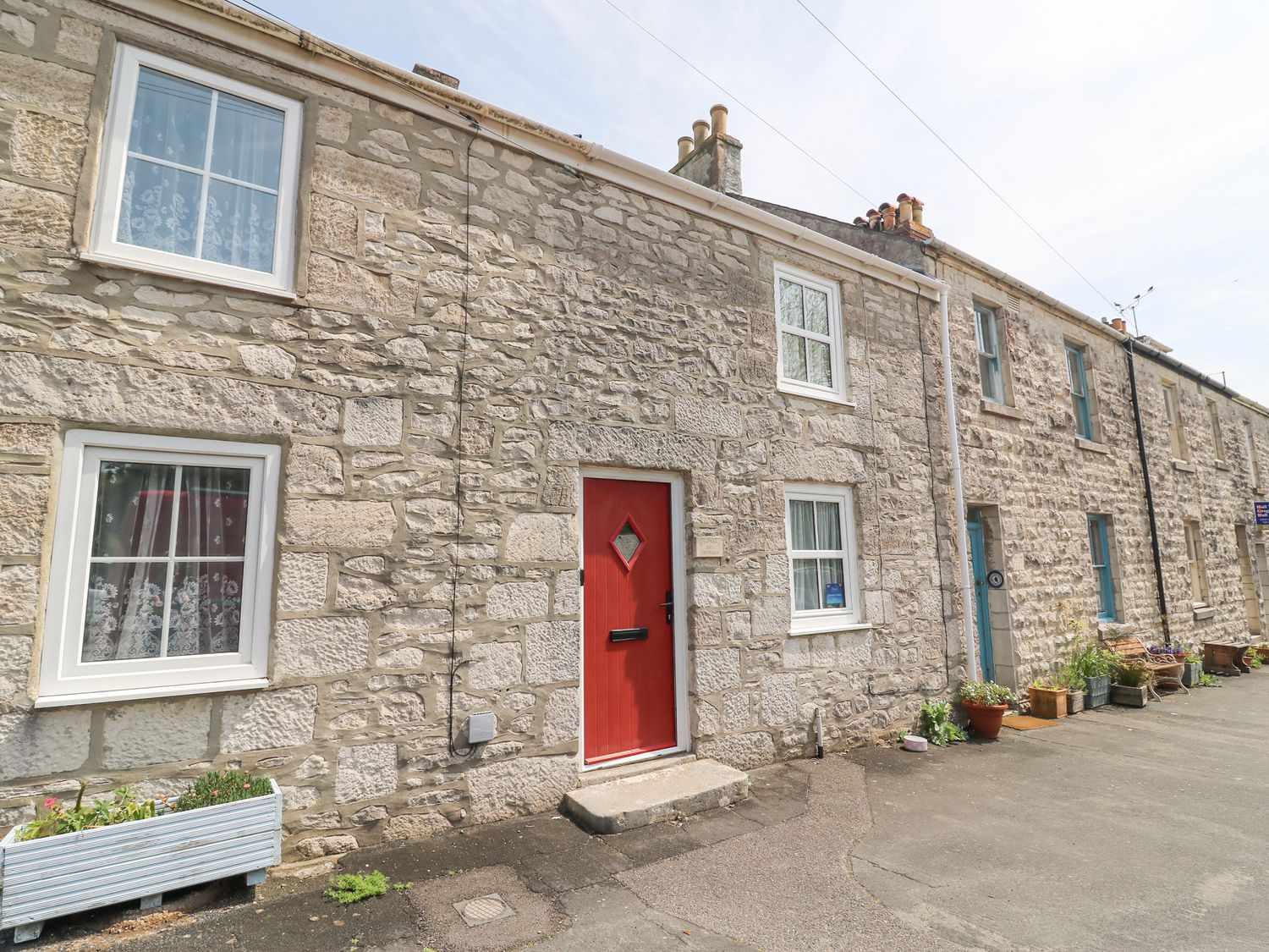 Stone terraced houses with white framed windows and a red door on a street at Bowman's Cottage Wakeham Portland