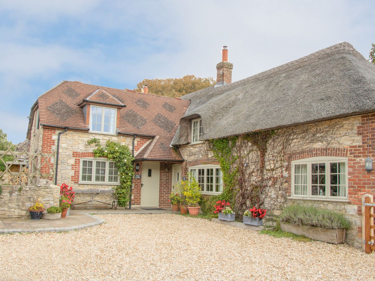 A stone and brick cottage with a thatched roof surrounded by plants and flowers at Forge Cottage in West Lulworth