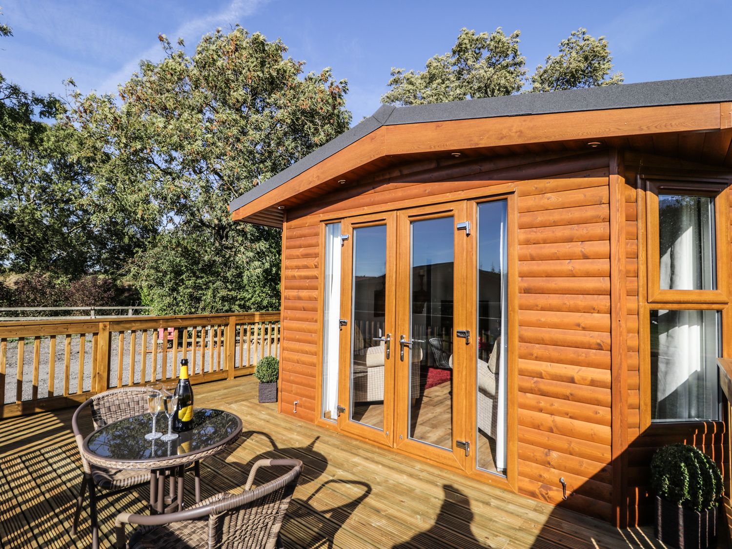 A wooden deck with a glass table and two wicker chairs outside a log cabin at Beech Tree Lodge in Stamford Bridge
