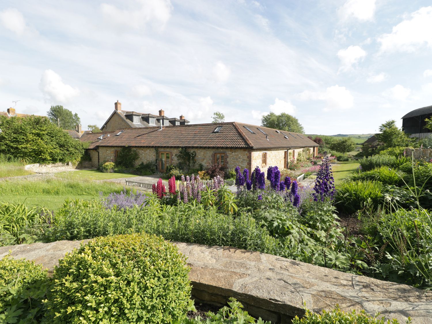 A garden with flowering plants and shrubs in front of a stone building with a tiled roof at Middle Farm Annex in Long Bredy