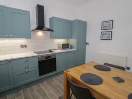 A kitchen with green cabinets a stove an oven a microwave and a wooden dining table with place mats at 2 Treborth Mews in Bangor