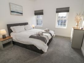 A bedroom with a double bed bedside tables lamps chest of drawers and two windows at 2 Treborth Mews in Bangor