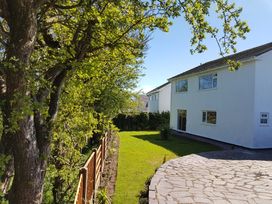 A backyard with green grass and a paved area next to a white two-story house at Anglesey White Haven in Llandegfan near Menai Bridge