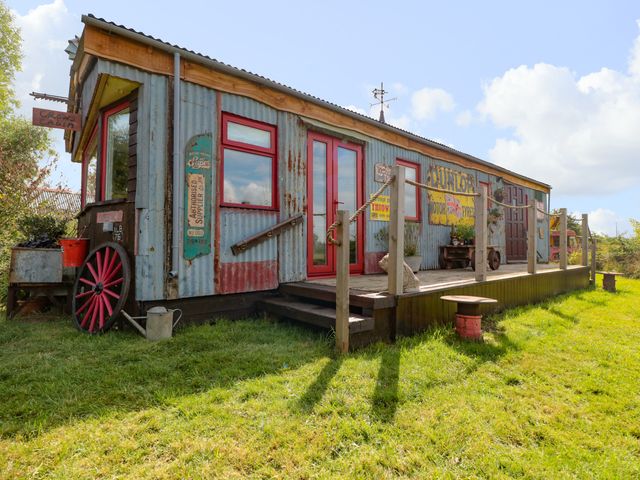 Exterior of a corrugated metal cabin with red windows and doors on a grassy lawn at Crows Cabin in Gloucester