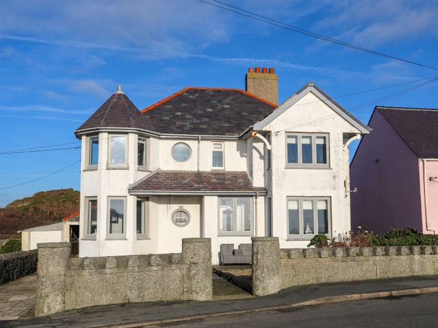 A two story white house with multiple windows a turret and a stone wall in front at Min Y Mor Trearddur Bay