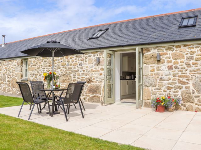 An outdoor patio with a table umbrella and four chairs next to a stone building with open double doors and flower pots at An Garth in Sennen
