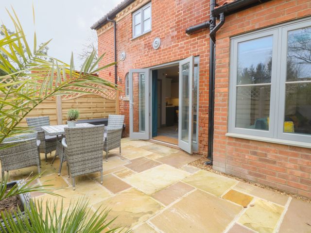 An outdoor patio with a dining table and six chairs next to a brick house with open French doors at The Old Rectory Coach House in Ashby St Mary near Rockland St Mary