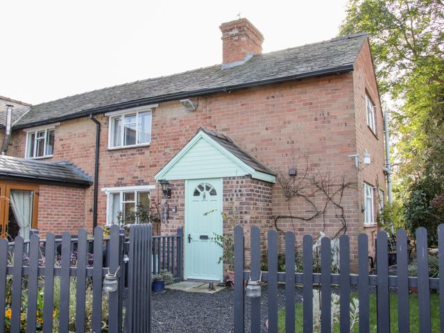 A brick cottage with a light blue front door and a wooden fence in front at Ensdon Lea Cottage in Ensdon near Nesscliffe