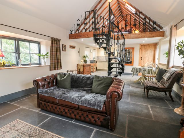 A living room with a leather sofa spiral staircase and dining table at Stable Cottage in Berwick-Upon-Tweed