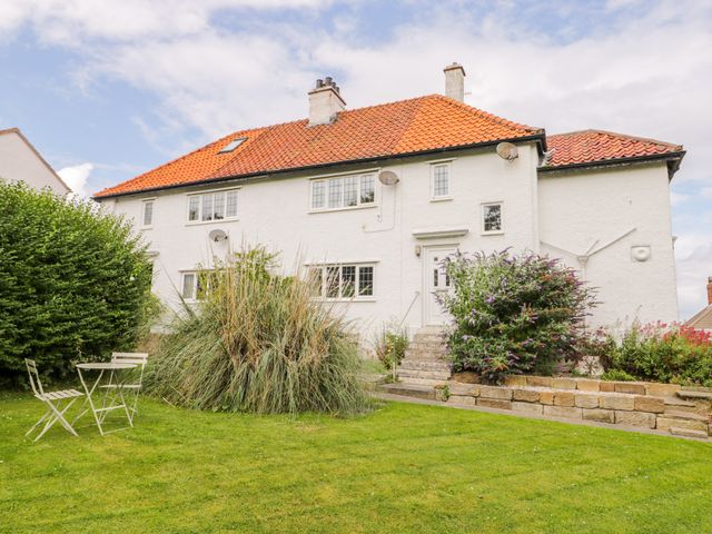 A white house with orange tiled roof a garden with grass bushes and a metal table with two chairs in front at Stakesby House Apartment 1 Whitby