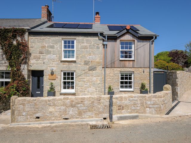 A stone cottage with solar panels on the roof and a stone wall in front at Stargazy Cottage in Praa Sands