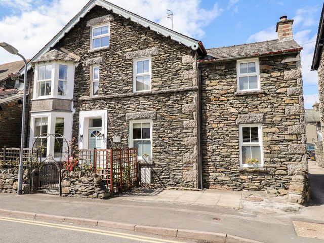 Stone house with white framed windows and a small garden behind a metal gate at The Postmasters House in Windermere