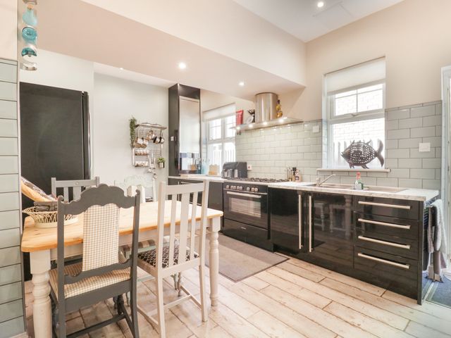 A kitchen with a wooden dining table and mixed chairs next to black cabinets and a window at Saxon Lodge Cottage in Felixstowe Suffolk