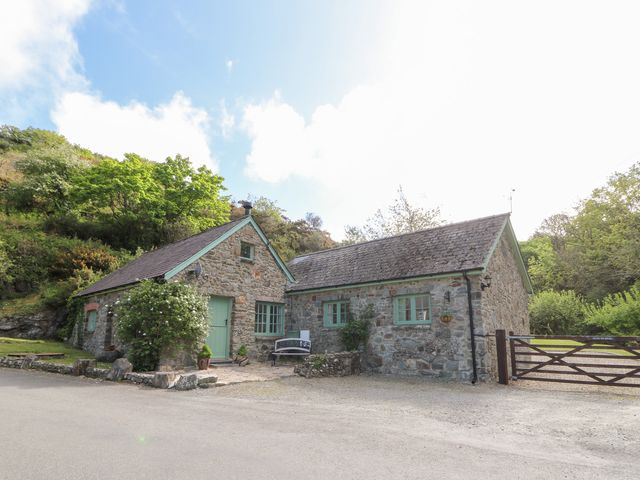 A stone cottage with green doors and windows next to a wooden gate surrounded by trees at Glyn Yr Efail in Moylegrove nr Newport and Cardigan