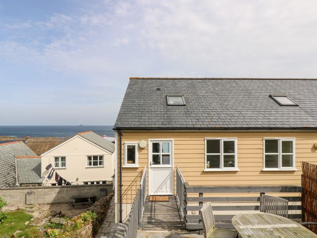 A yellow house with a wooden deck and outdoor furniture overlooking the sea at Pilchard Cottage in Sennen Cove