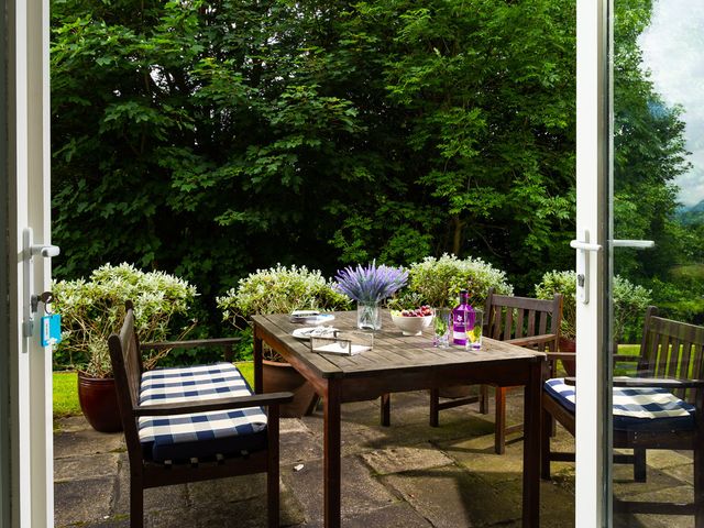 An outdoor patio with a wooden table and chairs with blue and white cushions and plants in pots at Tethera in Keswick