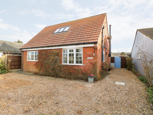 A brick house with a tiled roof a gravel driveway and a blue gate at Mermaids Purse in Eccles On Sea