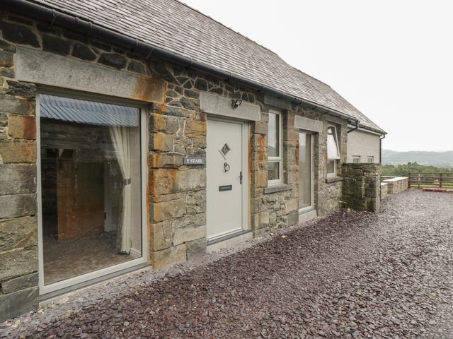 A stone house exterior with windows and a door on a gravel ground at Y Stabl in Llanddoged near Llanrwst